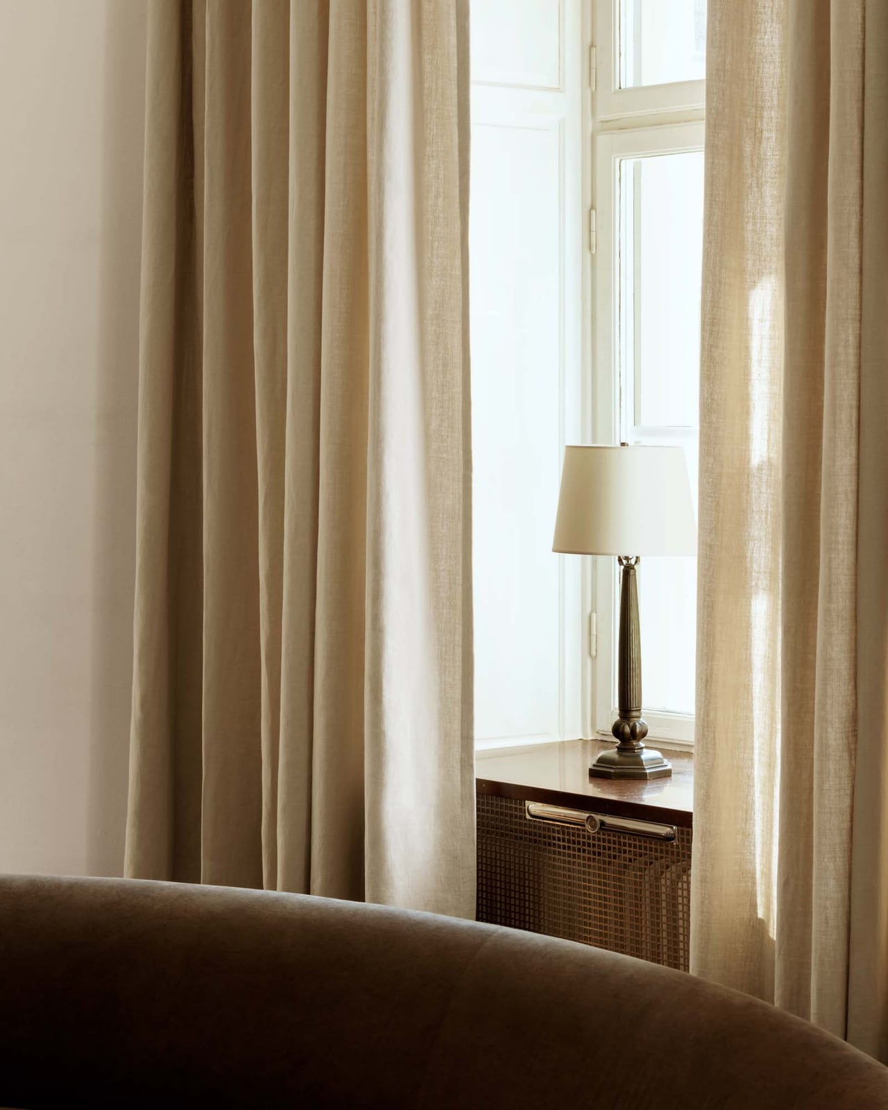 The Studio Linen curtain in Sand styled in a room, showing its heavyweight linen fabric and soft vertical folds.
