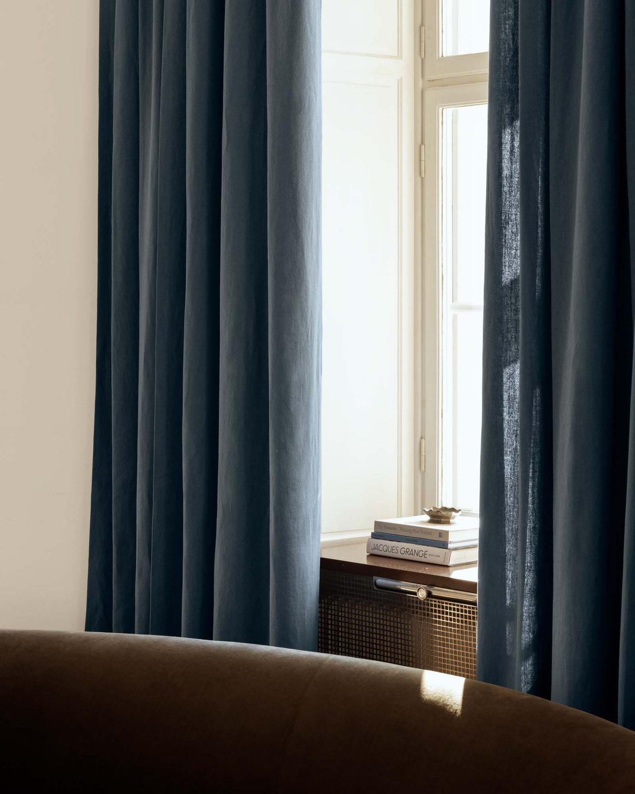 The Studio Linen curtain in Steel Blue styled by a window, featuring a heavy linen weave and soft vertical folds.