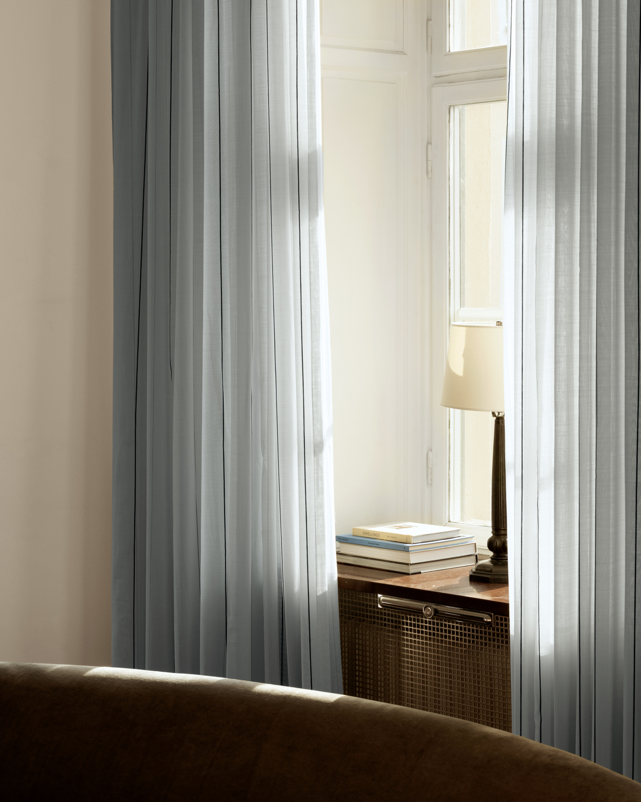 The Sheer Stripe curtain in Pale Blue/Black styled in a window with fine vertical stripes and a soft, light-filtering drape.